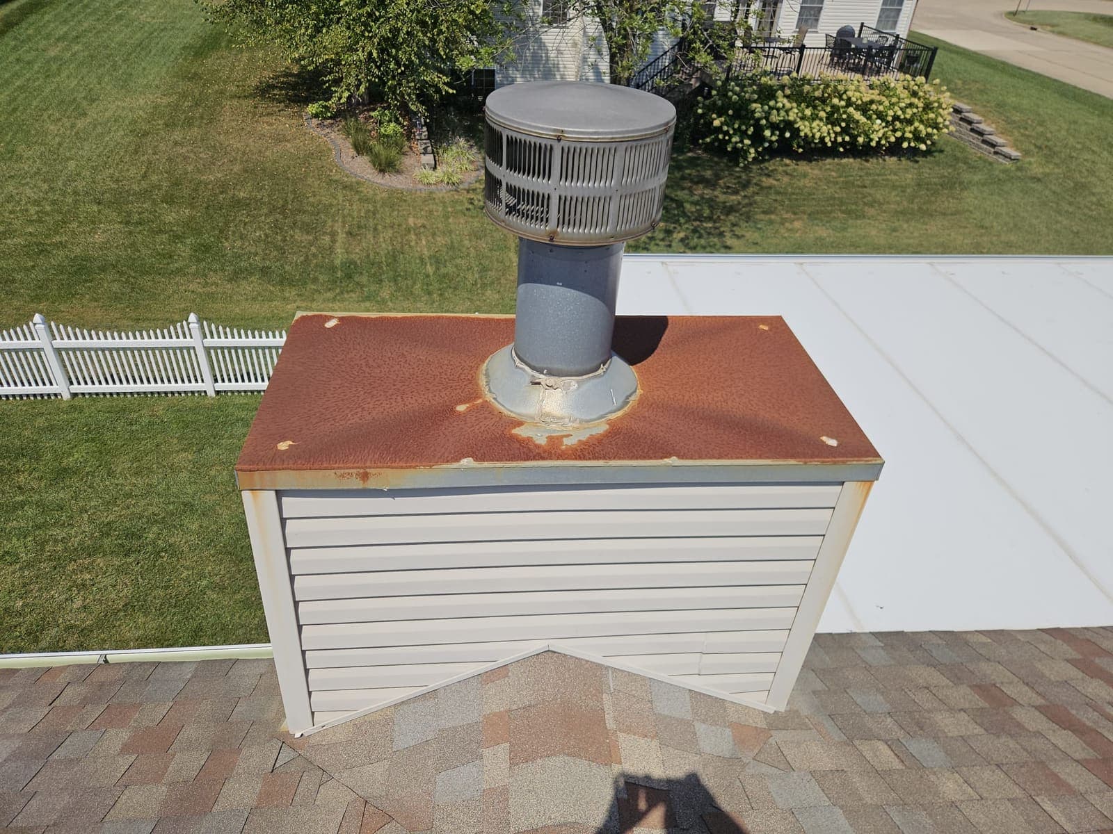 Rusted-through galvanised chase cover on a factory-built chimney chase, with rust bleeding around the flue collar and streaking down the vinyl siding